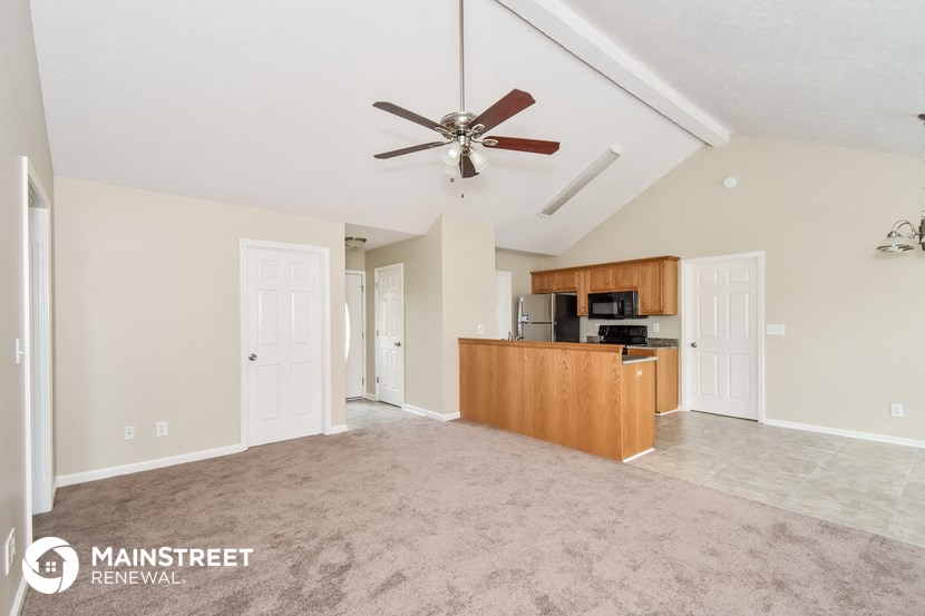 an empty living room with a kitchen and a ceiling fan