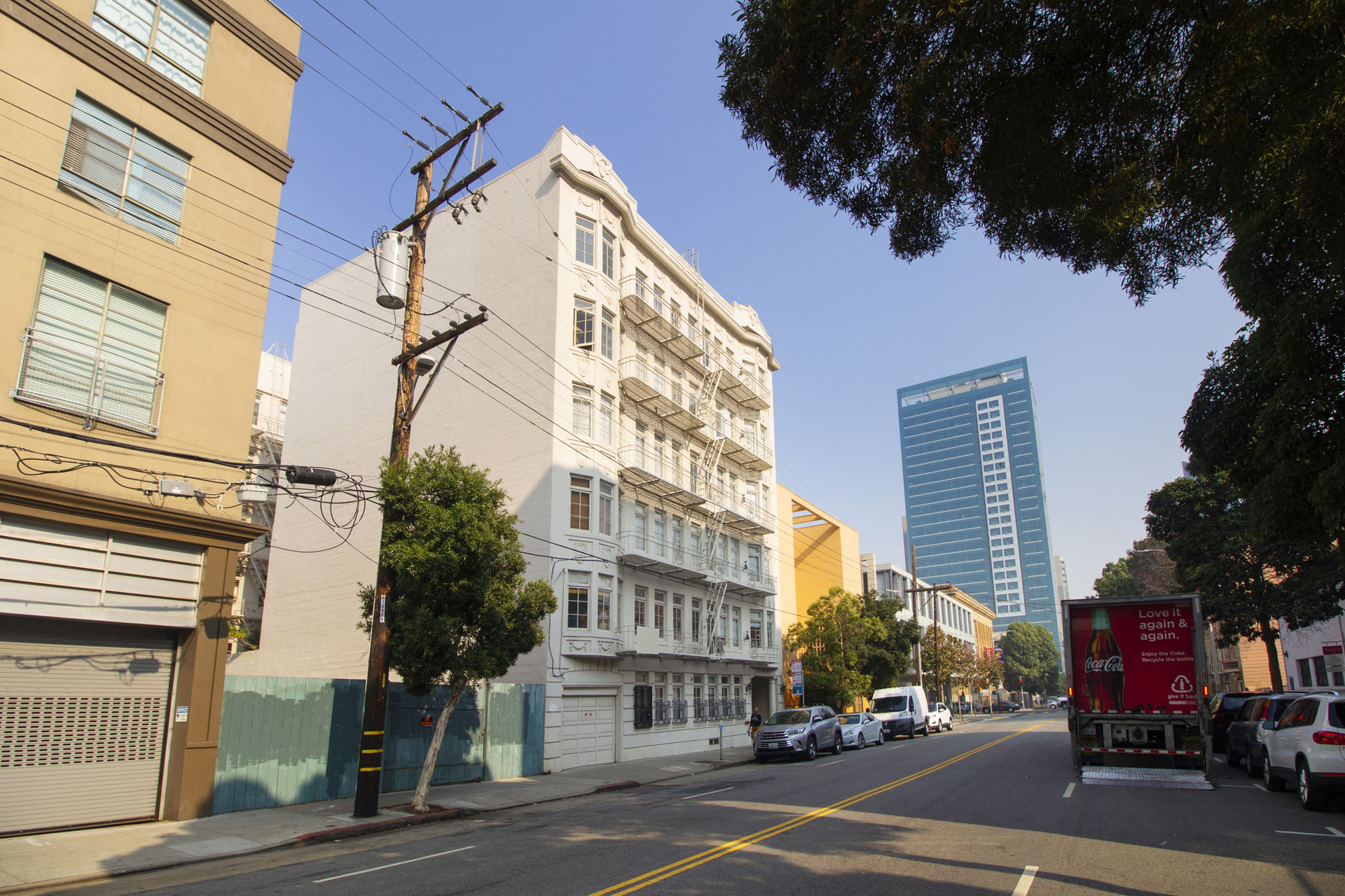A city street with cars parked on the side and a tall building in the background.