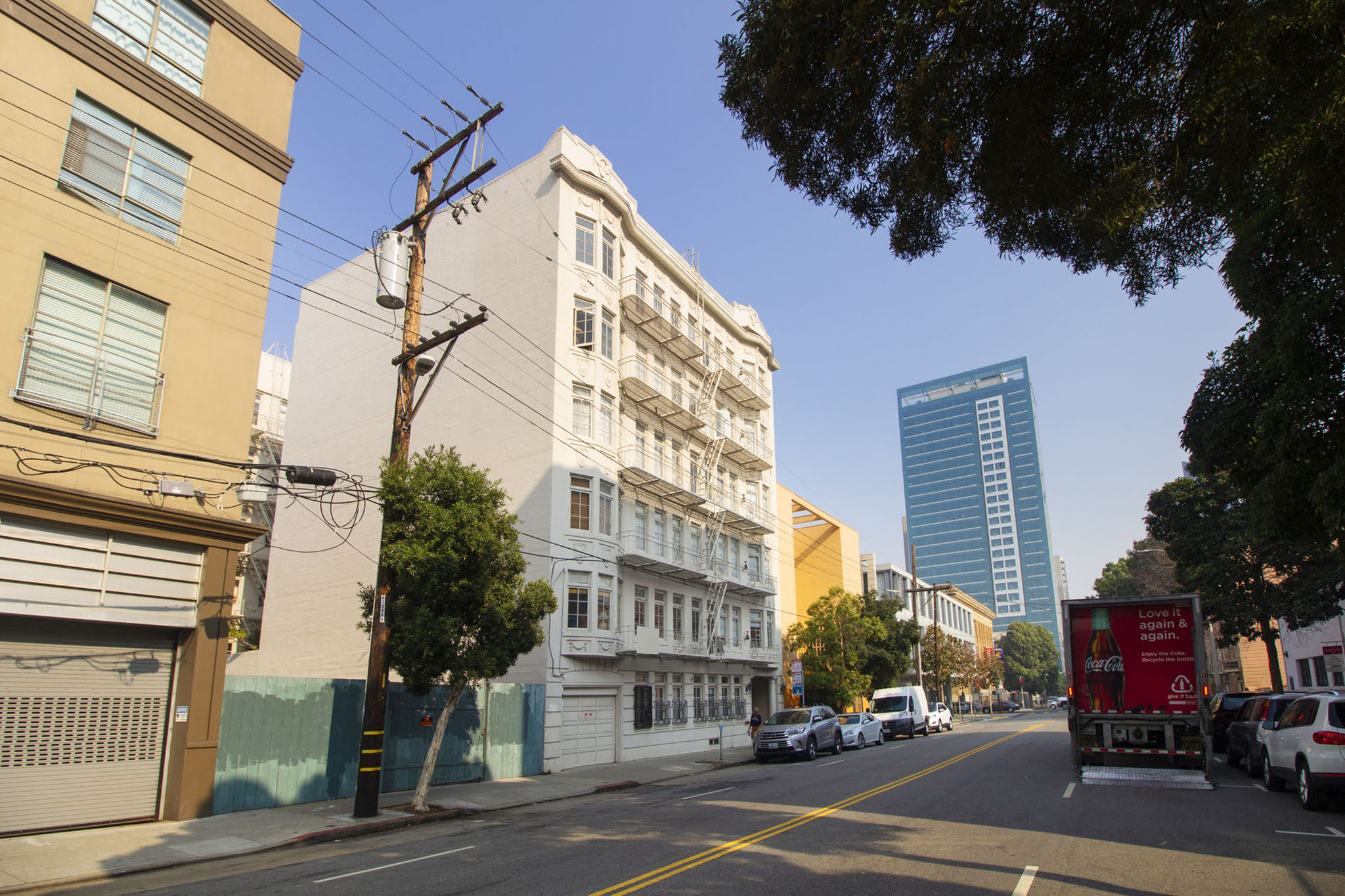 A city street with cars parked on the side and a tall building in the background.