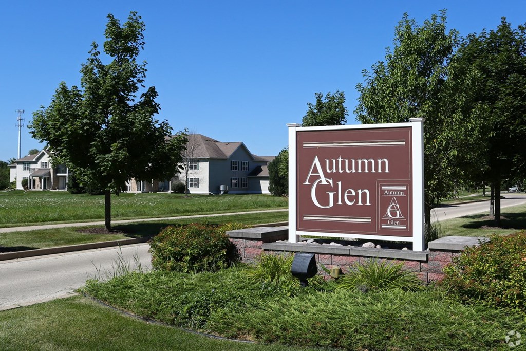 a sign for the autumn glen gas station in front of a street with houses
