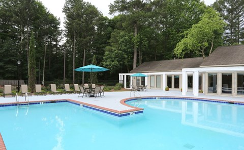A swimming pool with a blue umbrella and chairs around it.