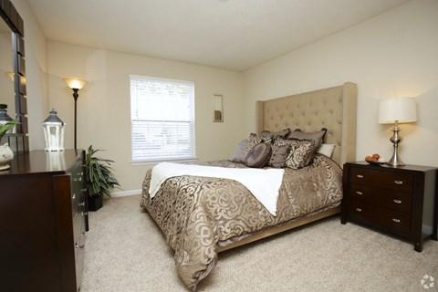 A bedroom with a large bed and a window with blinds.