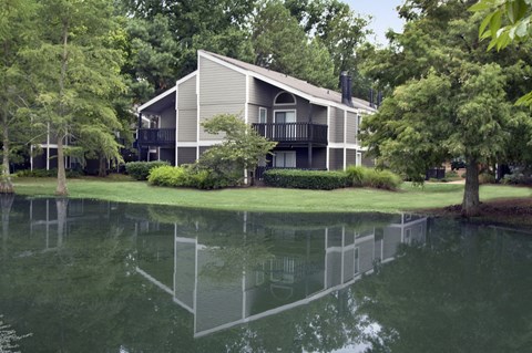 A house with a grey roof and a balcony is reflected in the water.