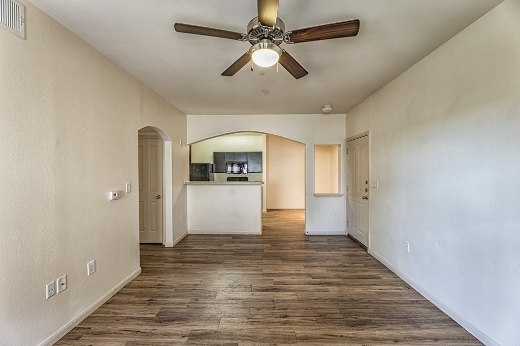 an empty living room with a ceiling fan and a kitchen