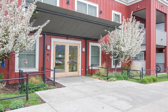 the front entrance of a red building with a sidewalk and trees