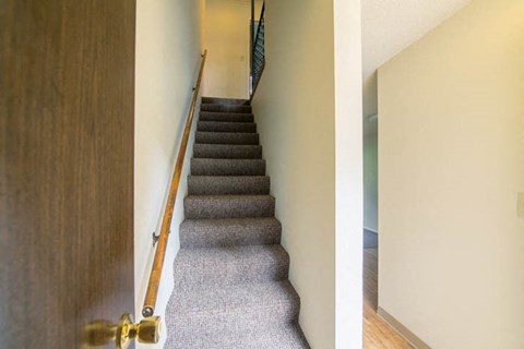 a staircase with a wooden railing and gray carpeted stairs