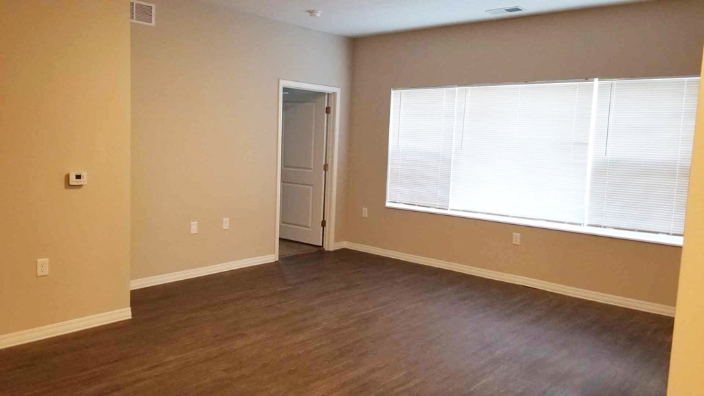 an empty living room with a large window and wooden floors