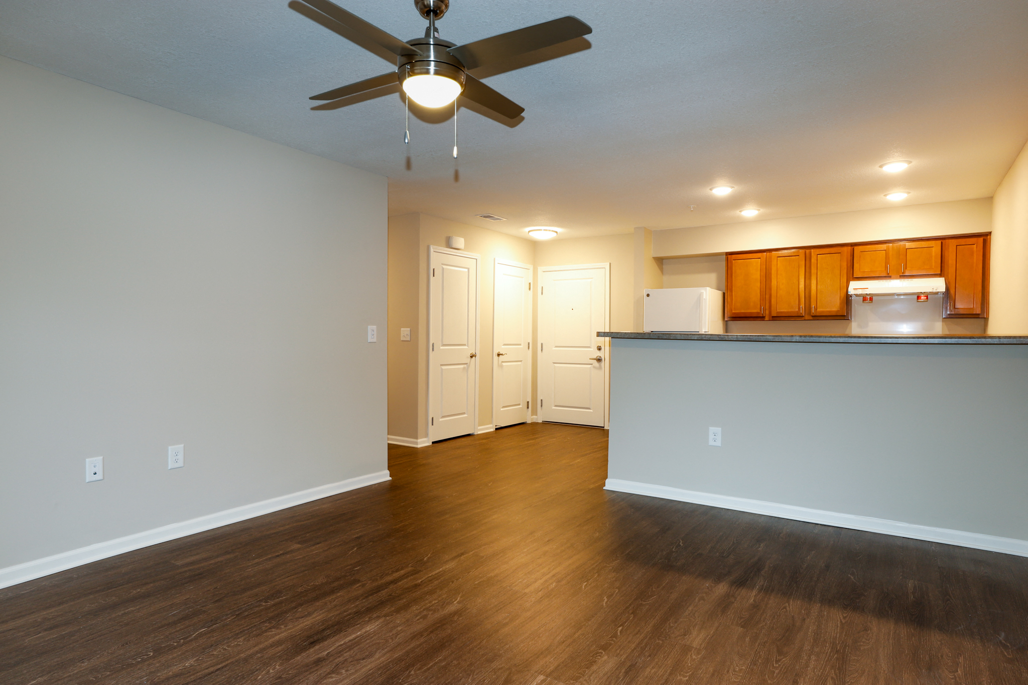 an empty living room with a ceiling fan and a kitchen