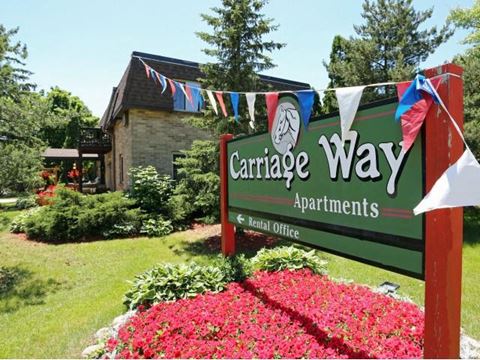 a sign for the carrage way apartments in front of a garden of flowers