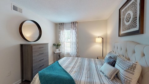 A bedroom with a bed, nightstand, lamp, and a mirror on the wall.