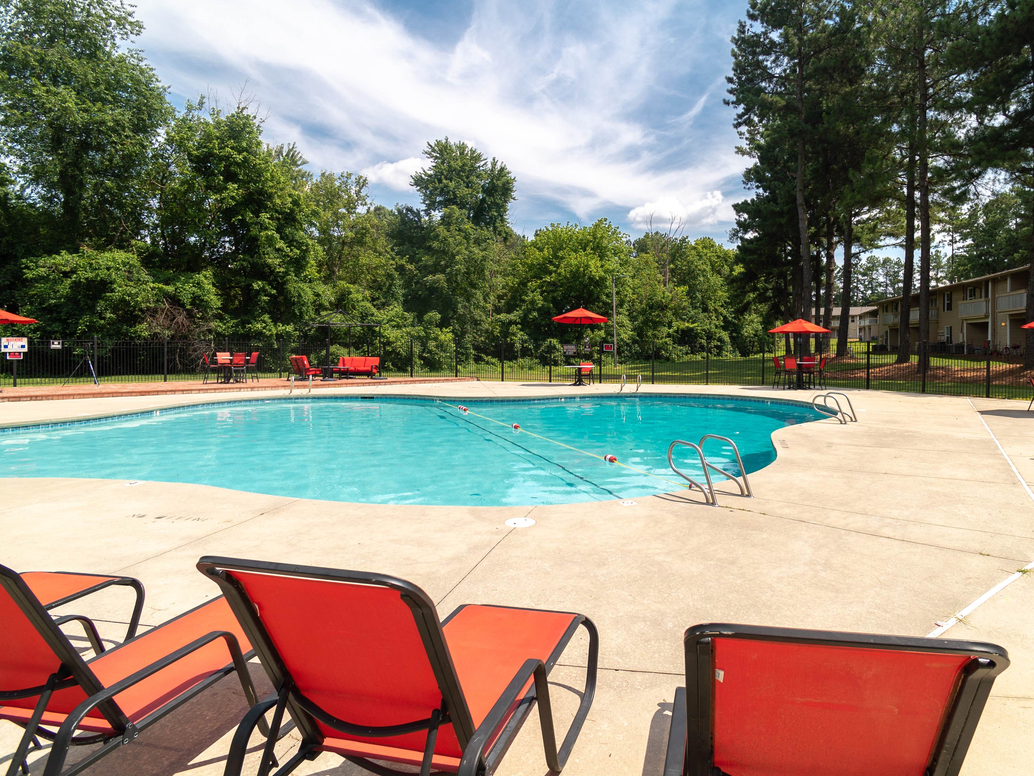 A pool with red chairs and trees in the background.