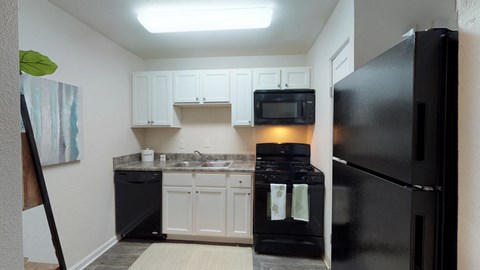 A black refrigerator sits in a kitchen with white cabinets.