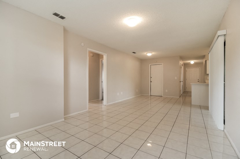 a spacious living room with a tiled floor and a door to the kitchen