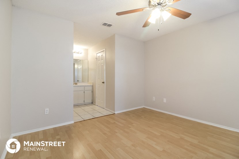 the spacious living room with hardwood flooring and a ceiling fan