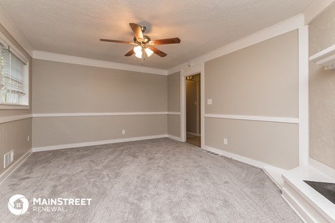 the spacious living room with carpet and a ceiling fan