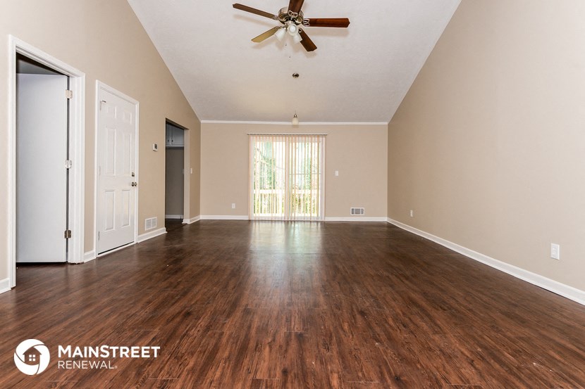 the spacious living room with hardwood flooring and a ceiling fan