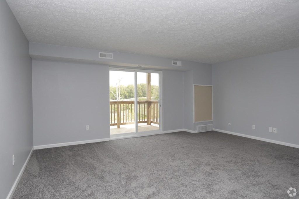 an empty living room with a sliding glass door to a balcony