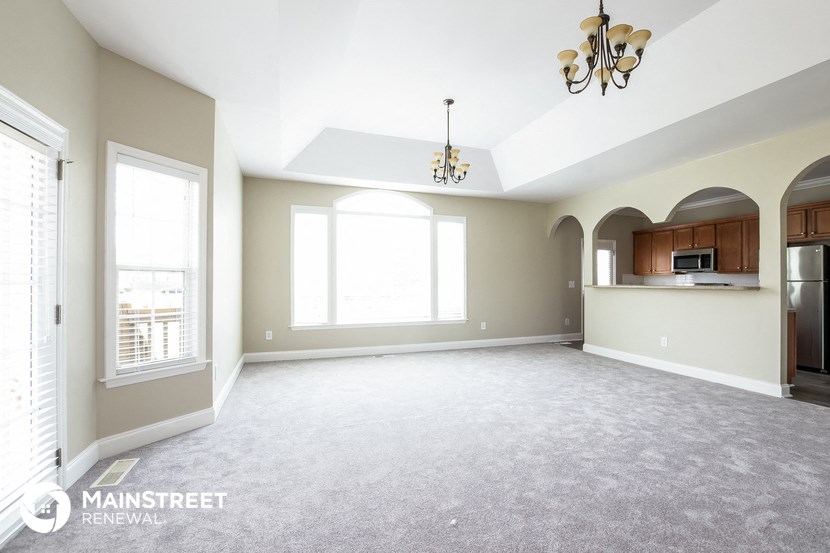 an empty living room with a kitchen and a large window
