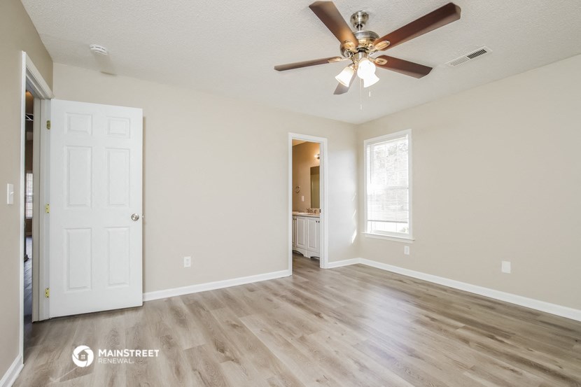an empty living room with a ceiling fan and a door to a bathroom