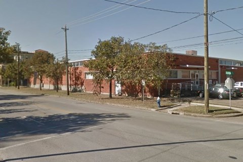 A street view with a red brick building on the right and a tree in the middle of the road.