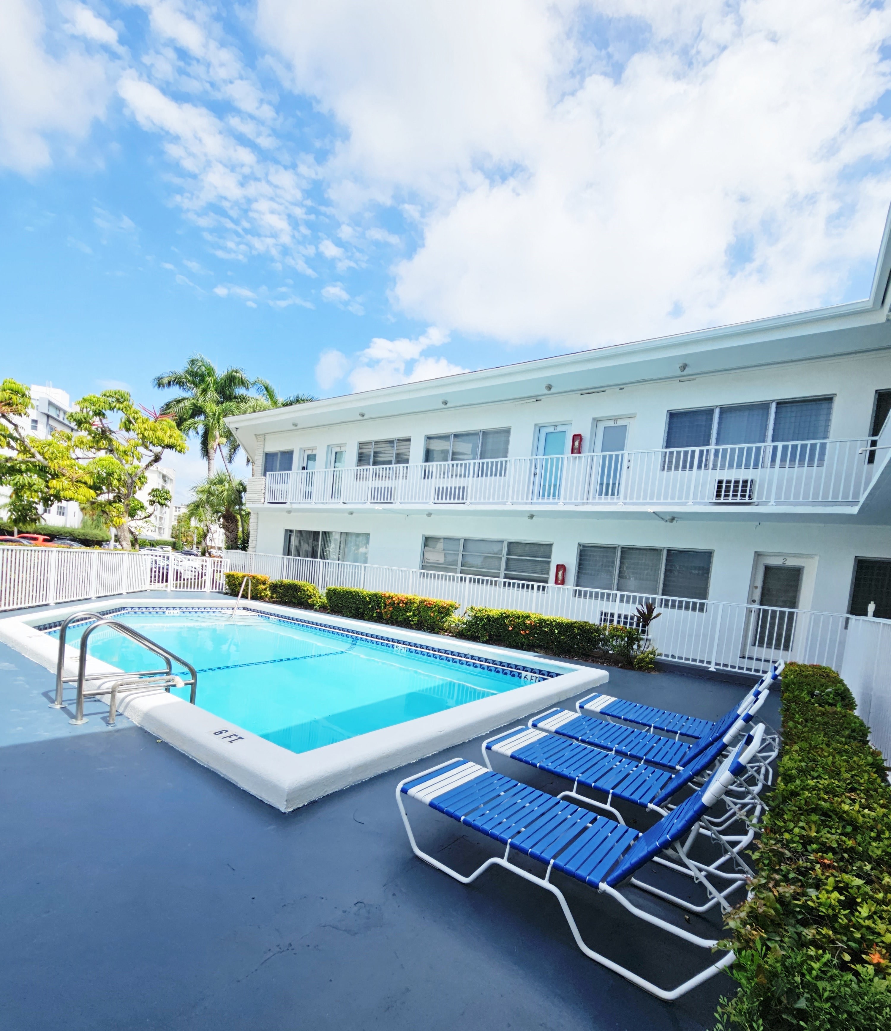 a large swimming pool in front of a building with blue lounge chairs