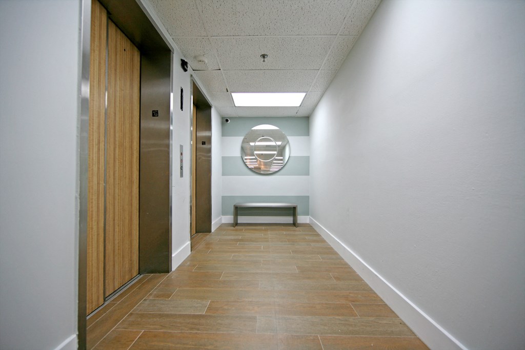 a hallway with a wood floor and white walls and a wooden door with a mirror
