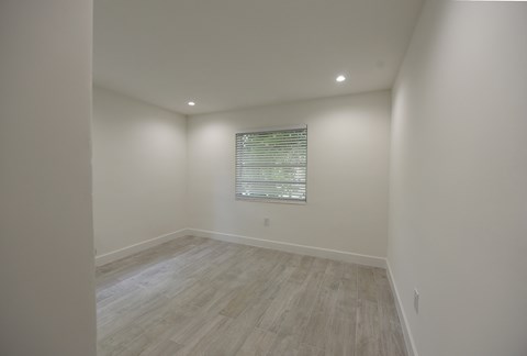 a bedroom with white walls and wood floors and a window