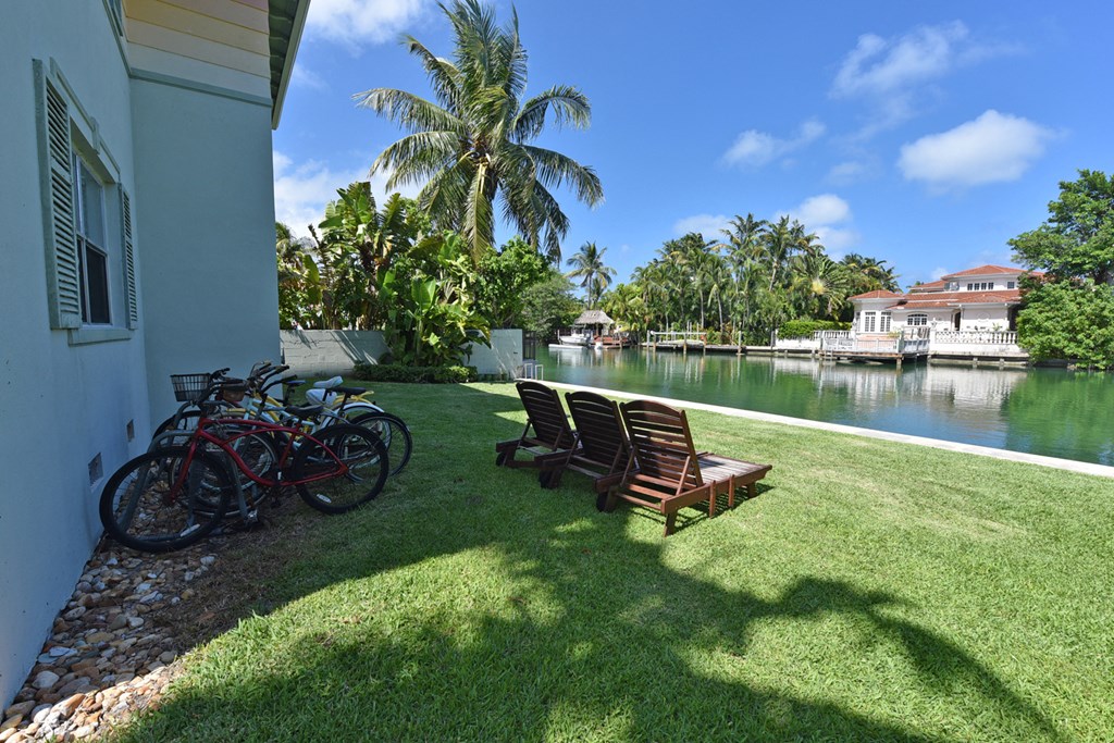 a yard with two chairs and a bike parked next to a house on the water