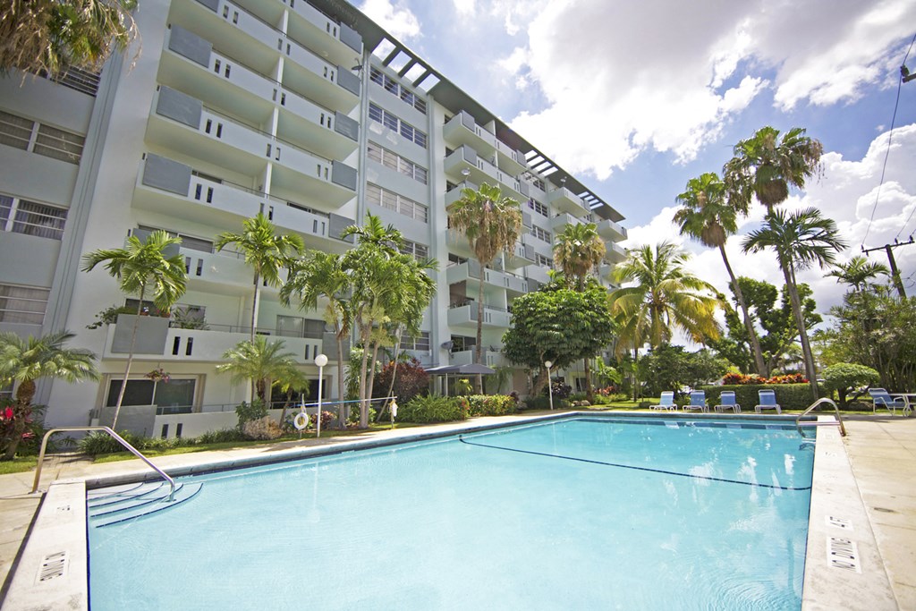 A swimming pool in front of a white apartment building with palm trees.