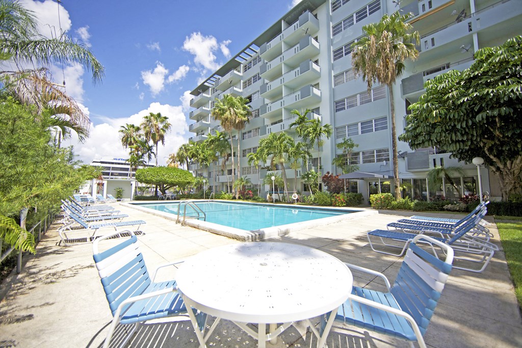 a large swimming pool with blue chairs and a white table in front of a building