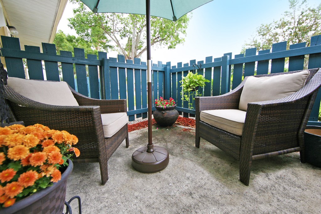 a patio with a blue fence and chairs and an umbrella
