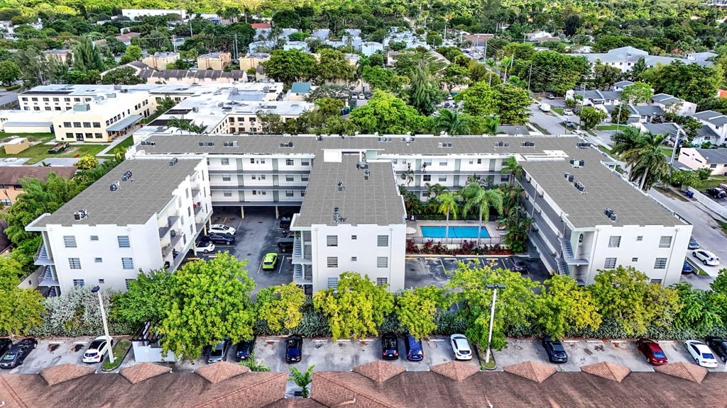 An aerial view of a white apartment complex with a pool and cars parked in the driveway.