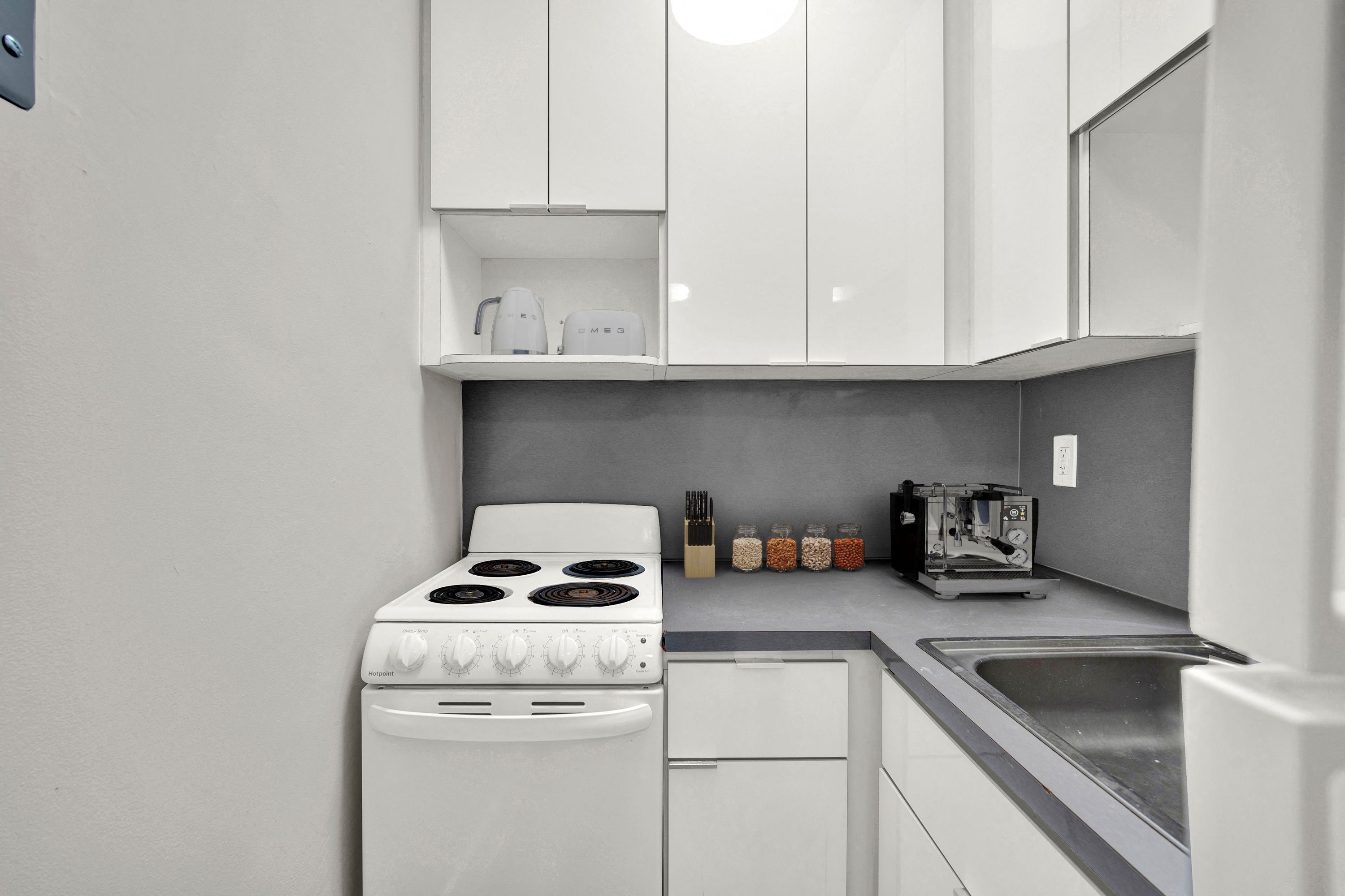 A white stove is in a kitchen with a white oven and white cabinets.