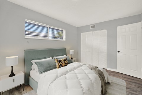 A bedroom with a large bed and a window with blinds.