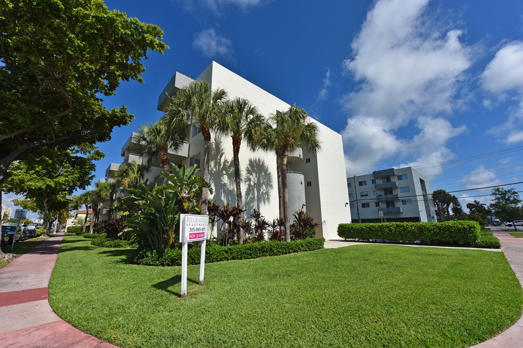 a white building with palm trees in front of it and a sign in the grass