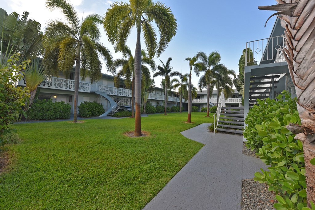 a courtyard with grass and palm trees and a building with stairs