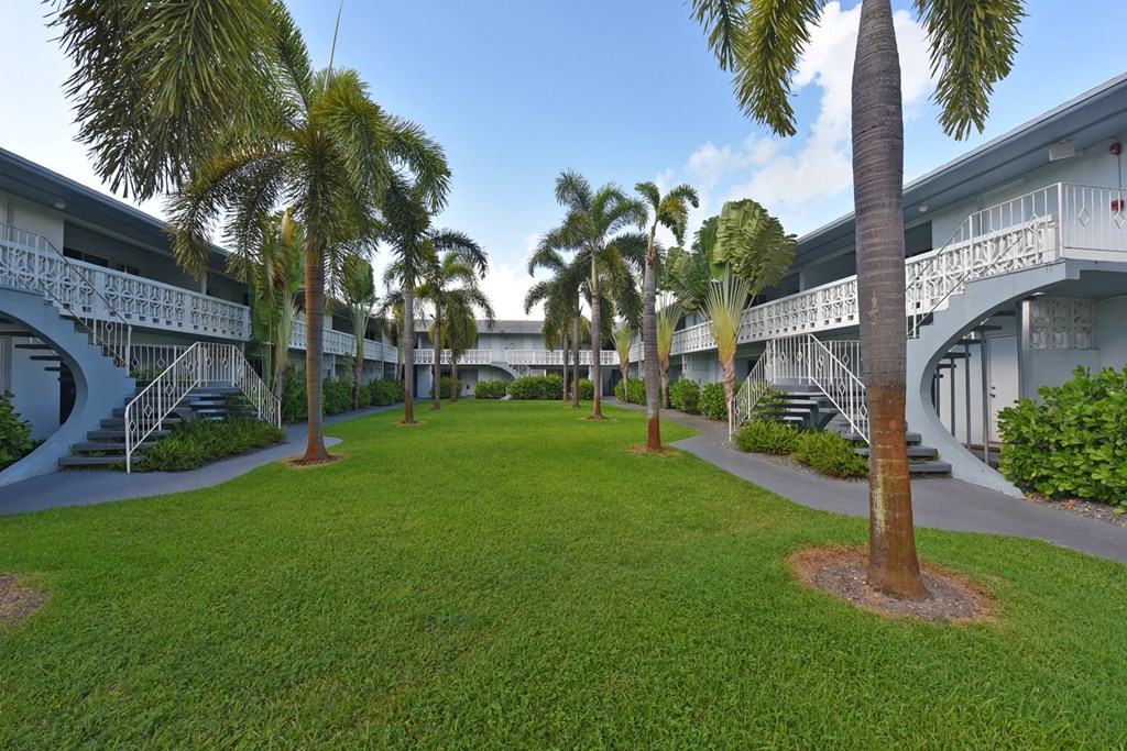 a grassy area with palm trees in front of a building