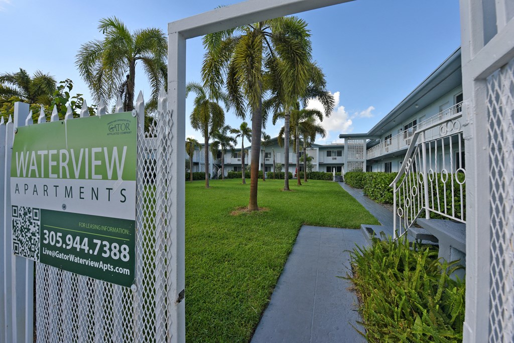 a sign for water view apartments in front of a lawn and palm trees