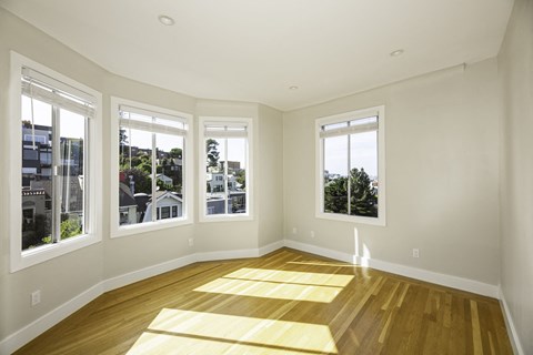 A sunny room with wooden floors and three windows.