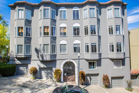 A grey building with a red tile roof and a car parked in front.