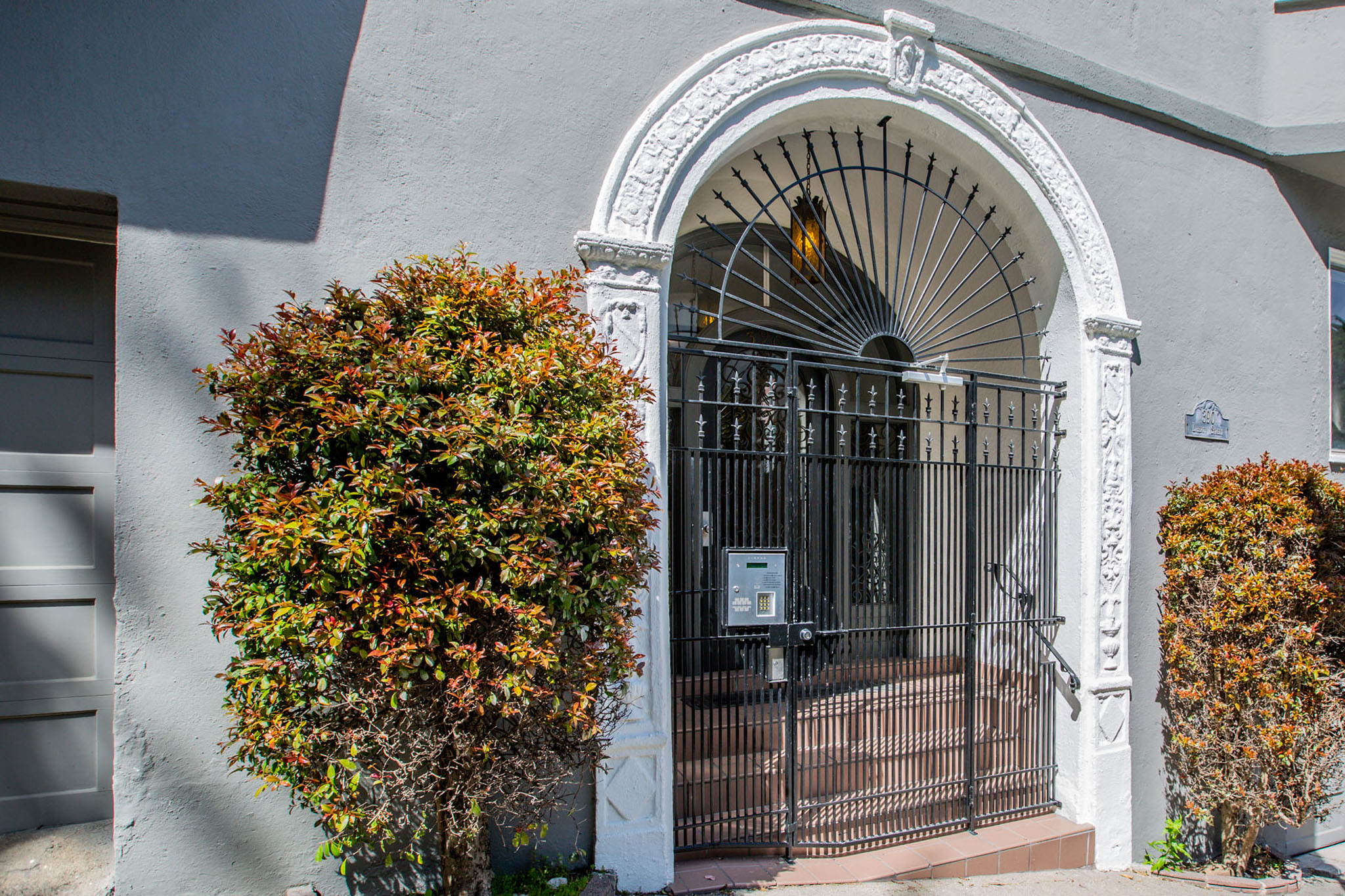A white arched doorway with a black gate and a small tree to the left.