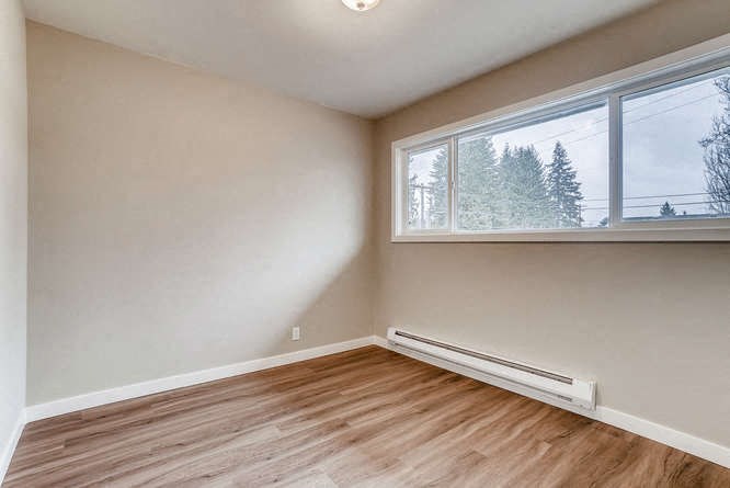 an empty bedroom with a large window and wood floors