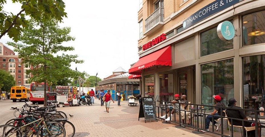 a city street with people sitting outside of a coffee shop