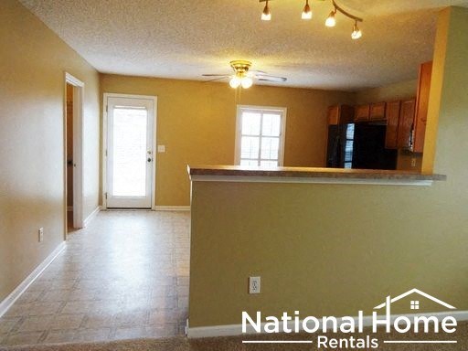 an empty living room with a kitchen and a ceiling fan