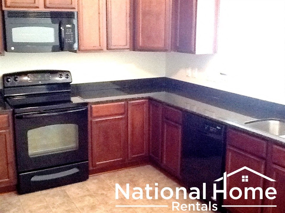 A kitchen with a black oven and microwave, wooden cabinets, and a logo for National Home Rentals.