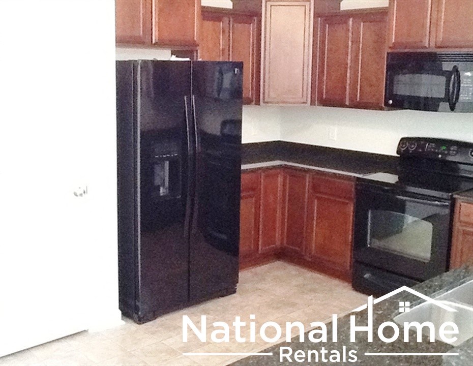 A black refrigerator and oven in a kitchen with brown cabinets.