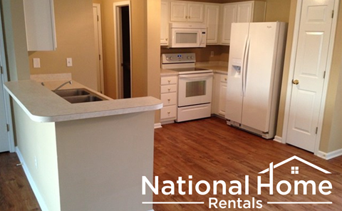 A kitchen with white appliances and a white refrigerator with the words National Home Rentals on the bottom.
