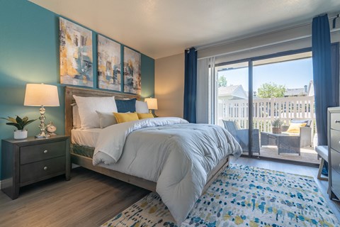 A bedroom with a large bed and a view of a fence and trees outside the window.
