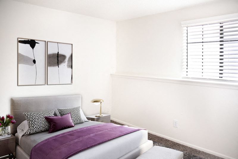 a bedroom with white walls and a bed with purple pillows