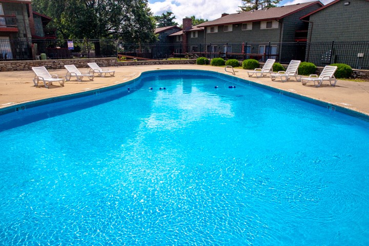 a large swimming pool with chairs and a building in the background
